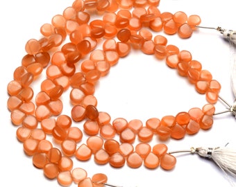 May include: A strand of orange sunstone beads, each bead is a flat, teardrop shape. The beads are strung on a silver wire and have white tassels at the ends.