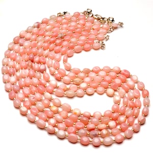 May include: Multiple strands of pink opal necklaces with gold-colored clasps and spacers. The oval-shaped beads have a soft, pastel pink hue, creating a delicate and feminine aesthetic. The necklaces are arranged in a cascading pattern.