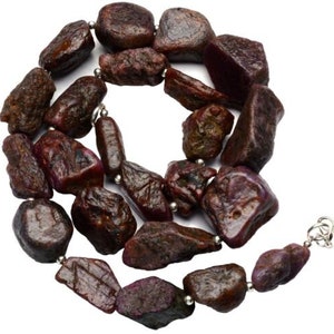 May include: A strand of dark red ruby gemstone beads, each bead is irregularly shaped and has a rough, natural texture. The beads are strung on a silver chain with silver clasps.