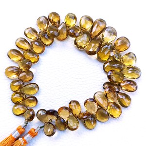 May include: A strand of golden brown gemstone beads in a teardrop shape. The beads are arranged in a circle with a tassel at the bottom.