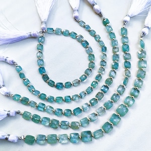 Puede incluir: Un conjunto de seis hebras de cuentas de piedras preciosas azul verdosas. Las cuentas son de forma cuadrada y tienen un acabado facetado. Cada hebra tiene un borla blanca en un extremo.