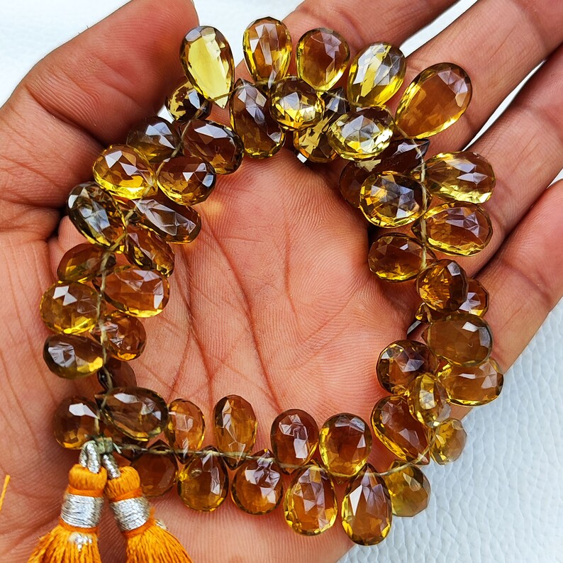 May include: A strand of faceted, teardrop-shaped, golden brown gemstone beads. The beads are strung on a thin cord and have a tassel at the end.