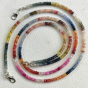 Puede incluir: Un collar de cuentas multicolor con pequeñas cuentas de piedras preciosas facetadas en un degradado de tonos rosa, rojo, naranja, amarillo, verde y azul. El collar está rematado con un cierre de mosquetón de metal plateado en cada extremo.