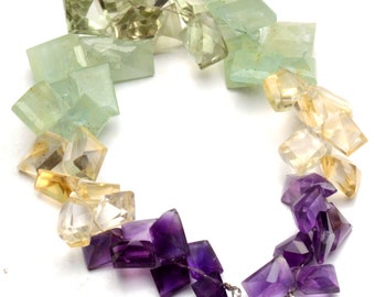 May include: A multi-colored gemstone necklace with green, yellow, and purple faceted beads. The necklace has two white tassels at the end.