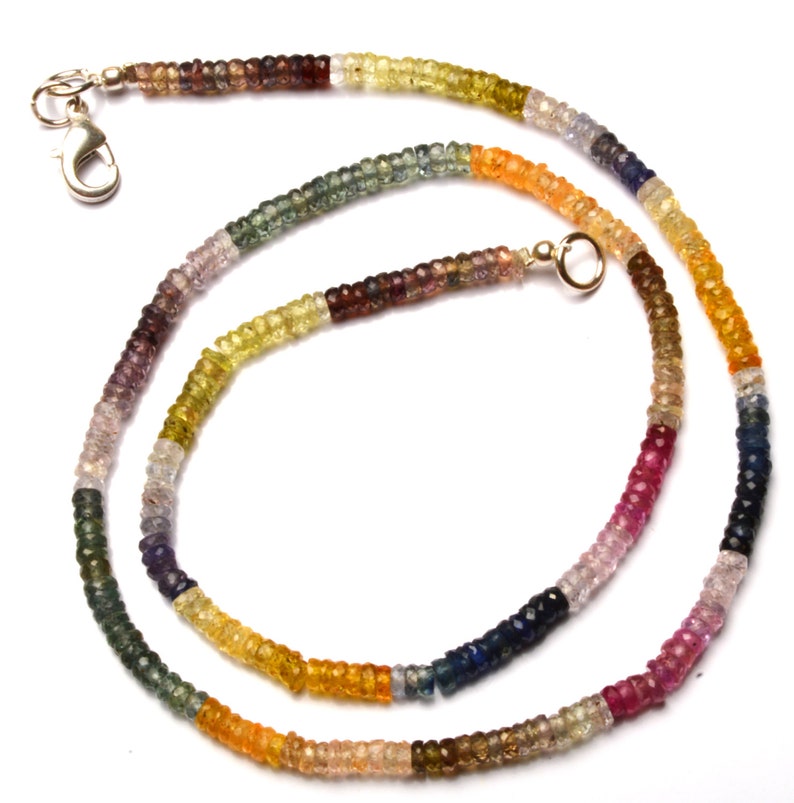 Puede incluir: Un collar de piedras preciosas multicolores con un cierre plateado y un conector dorado. El collar est&aacute; hecho de peque&ntilde;as cuentas redondas en tonos de azul, verde, amarillo, naranja, rojo y marr&oacute;n.
