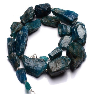 Puede incluir: Un collar hecho de piedras de apatita azul verdoso sin pulir enhebradas en alambre de plata. Las piedras son de forma y tama&ntilde;o irregulares, lo que le da al collar un aspecto natural y terroso.