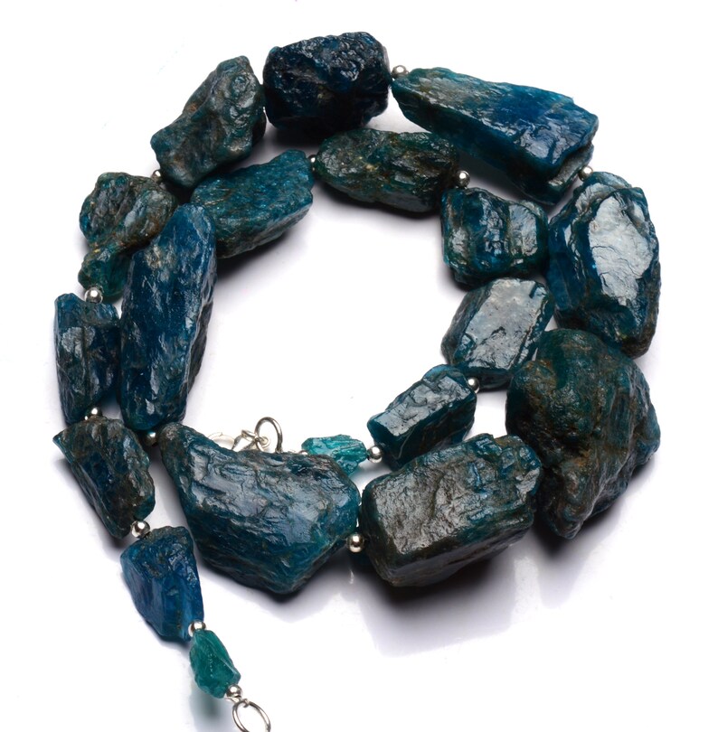 Puede incluir: Un collar hecho de piedras de apatita azul verdoso sin pulir enhebradas en alambre de plata. Las piedras son de forma y tama&ntilde;o irregulares, lo que le da al collar un aspecto natural y terroso.