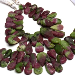 Op de afbeelding: Een streng groene en roze edelsteen kralen, met een druppelvorm. De kralen zijn geregen op een draad en hebben aan elk uiteinde een kwast.