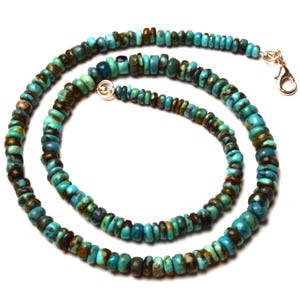May include: A turquoise beaded necklace with a silver clasp. The necklace features small, rounded beads in shades of turquoise and brown. The beads are strung together to form a necklace.