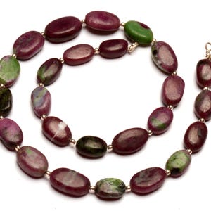 Op de afbeelding: Een ketting gemaakt van ovale groene en roze edelsteen kralen. De kralen zijn geregen aan een gouden ketting.
