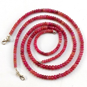 May include: A long strand of pink gemstone beads with silver clasps. The beads are small and round, and the necklace is layered in a coil.