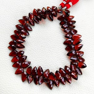 Könnte beinhalten: Eine Kette aus tief roten Edelsteinperlen, jede Perle ist facettiert und tropfenförmig. Die Perlen sind auf einer dünnen Schnur aufgefädelt und in einem Kreis angeordnet.