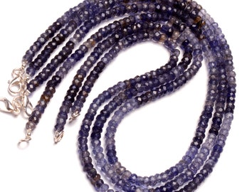 May include: A strand of blue and gray gemstone beads, with a faceted finish, strung on a silver chain. The beads are arranged in a circular pattern, with the chain extending out from the center.