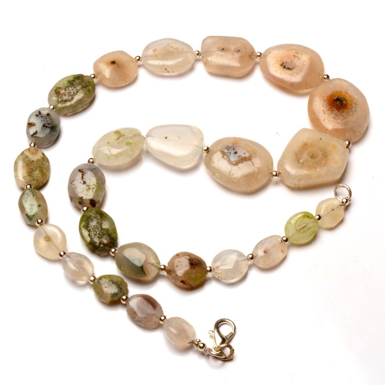 May include: A necklace featuring a variety of irregularly shaped, polished stone beads in shades of beige, green, and brown. The beads are strung together with small silver-colored metal beads and a clasp.