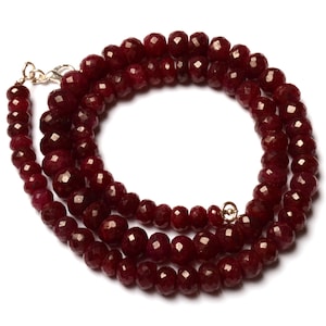 Op de afbeelding: Een dubbele ketting van facetgeslepen robijn kralen. De ketting is gemaakt van donkerrode kralen en heeft een zilveren sluiting.