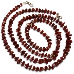 Op de afbeelding: Een lange ketting en een kortere armband gemaakt van kleine, onregelmatige, rode robijn kralen geregen aan een gouden ketting.