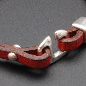 May include: A red leather bracelet with a silver clasp and a silver bead. The clasp is a hook and eye style.