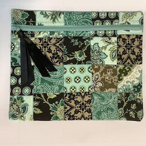 May include: A rectangular patchwork pouch with a teal zipper and black ribbon pull. The fabric features a mix of floral and paisley patterns in shades of green, brown, and teal. The pouch is quilted.