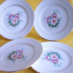 Puede incluir: Juego de cuatro platos de cena de cerámica blanca con una superficie texturizada en relieve. Cada plato presenta un borde dorado y un diseño floral con flores rosas, blancas y verdes.