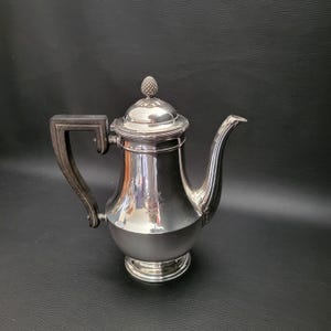 May include: A silver coffee pot with a black wooden handle and a decorative finial on the lid.