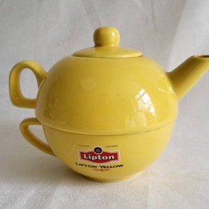 Könnte beinhalten: Ein gelber Keramik-Teekannen- und Tassen-Set mit einem roten Lipton-Logo und dem Text "Lipton Yellow" auf der Unterseite.