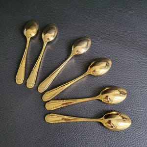 Peut inclure: Six cuillères dorées avec un bord décoratif. Les cuillères sont disposées sur une surface sombre. Les cuillères ont une surface brillante et réfléchissante.
