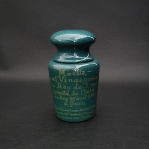 Puede incluir: Una botella de cerámica verde azulada con una inscripción dorada que dice "Maille, Seul Vinaigrier du Roy de l'm, Provote de l'hotel du Roy 27 aout 1769, a Paris. Maille, des trois Herbes Verts, Mostarde Verde au Vin et Aromatisation aux Herbes".