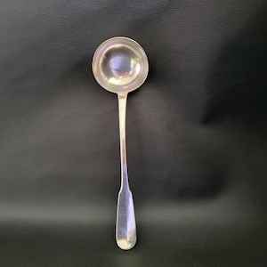 May include: A silver ladle with a round bowl and a long, slender handle. The ladle is made of a shiny, reflective metal and is designed for serving soups, sauces, or other liquids. The handle has a slightly flattened end.