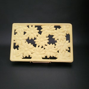 Op de afbeelding: Een gele keramische onderzetter met een bloemenpatroon. De onderzetter is rechthoekig en heeft een reliëf van bloemen.