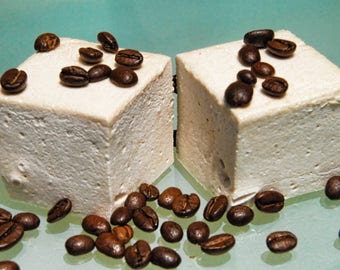 May include: Two white square-shaped marshmallows topped with coffee beans on a light blue surface.