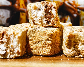 May include: A close-up of a stack of graham cracker squares with marshmallow and chocolate filling. The squares are covered in a layer of graham cracker crumbs.