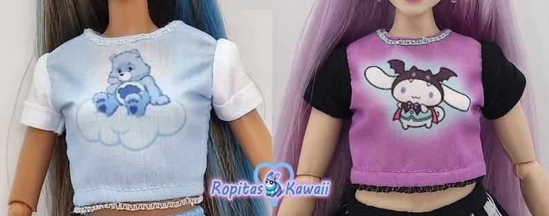 K&ouml;nnte beinhalten: Zwei Puppenoberteile: eines hellblau mit einem Care Bear auf einer Wolke, das andere lila mit einer Zeichentrickfigur im Fledermauskost&uuml;m. Beide Oberteile haben kurze &Auml;rmel und dekorative Verzierungen.