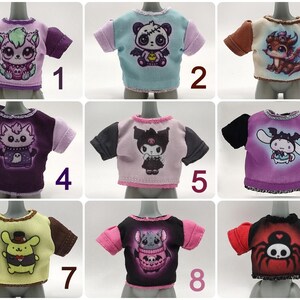 K&ouml;nnte beinhalten: Neun puppenkleine T-Shirts mit verschiedenen Cartoon-Charakter-Designs. Jedes Shirt hat eine andere Grafik, darunter ein Panda, ein Drache, eine Katze und eine Spinne. Die Shirts haben kurze &Auml;rmel und sind in verschiedenen Farben wie Lila, Rosa und Schwarz erh&auml;ltlich.