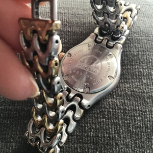 May include: A silver and gold watch with a stainless steel band. The watch face is obscured, but the back of the watch has the word "ellesse" printed on it.