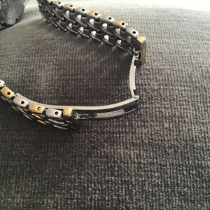 May include: A two-tone watch band with a silver and gold metal design. The band has a clasp closure.