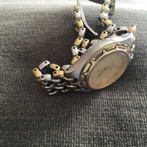May include: A two-tone gold and silver wristwatch with a round face and a metal band.