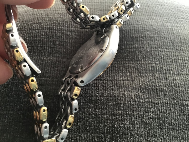 May include: A silver and gold two-tone watch with a stainless steel band. The watch has a round face and a silver case. The band is made of interlocking links.