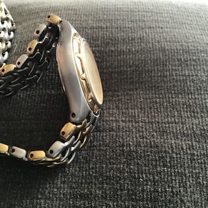 May include: A two-tone gold and silver watch with a metal band. The watch has a round face and a gold bezel.