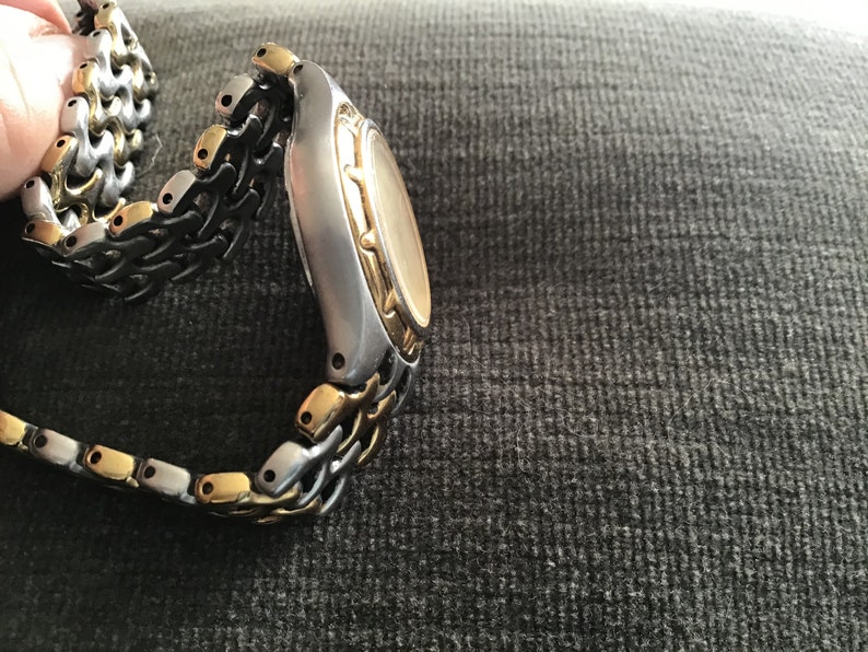 May include: A two-tone gold and silver watch with a metal band. The watch has a round face and a gold bezel.