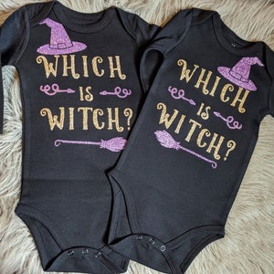 May include: Two black long-sleeved baby onesies with the text "Which is Witch?" in gold glitter and a purple glitter witch hat and broom.