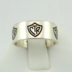 Op de afbeelding: Een zilveren bandring met drie zwarte schildvormige gravures van de letters "CTR".