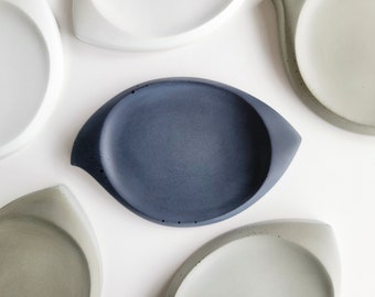 Könnte beinhalten: Ein Set aus fünf Beton-Schalen in verschiedenen Grautönen, darunter eine dunkelblaue Schale. Die Schalen sind alle oval geformt und haben einen leicht erhöhten Rand.