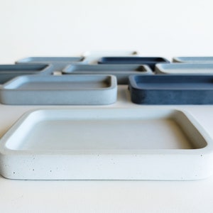May include: A set of six rectangular concrete trays in various shades of gray. The trays are arranged in a staggered pattern, with the largest tray in the foreground.