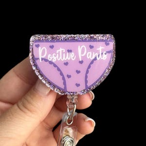 May include: Purple glitter badge holder with a pink and purple cartoon image of underwear with the text "Positive Pants".