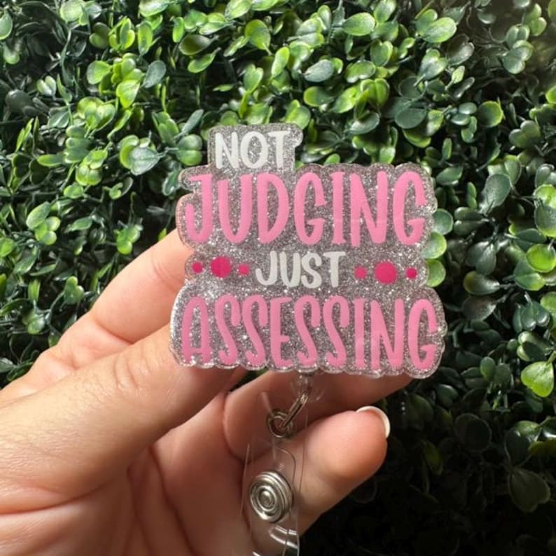 May include: A pink and silver glitter badge holder with the text "NOT JUDGING JUST ASSESSING".