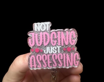 May include: Pink and white glitter badge holder with the text "Not Judging Just Assessing".