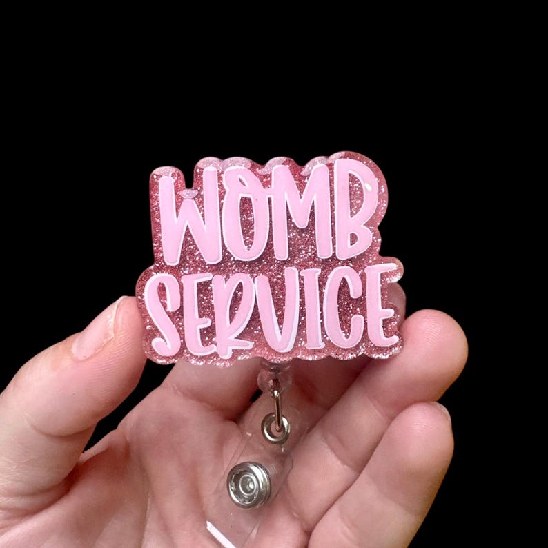 May include: Pink glitter badge holder with the text "WOMB SERVICE" in white lettering.