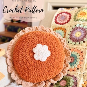 May include: A round, orange crochet pillow shaped like a pie with a light tan ruffled crust and a white flower-shaped center. Text on the image reads: THE CUTIE PIE PILLOW Crochet Pattern INSTANT PDF DOWNLOAD and EAT PRAY & CROCHET.