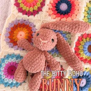 May include: A crocheted pink bunny toy with black eyes and a white stitched nose rests on a colorful granny square blanket. The blanket features various floral patterns in shades of pink, orange, blue, and green. Text on the image reads "THE BITTY BOHO BUNNY PDF CROCHET PATTERN."