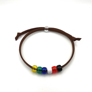 May include: A brown leather bracelet with six colorful beads: yellow, green, blue, white, red, and black. The bracelet has an adjustable sliding knot closure. The beads are evenly spaced along the bracelet's circumference.